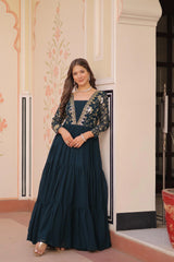 Woman in a dark blue gown with floral embroidery standing indoors.