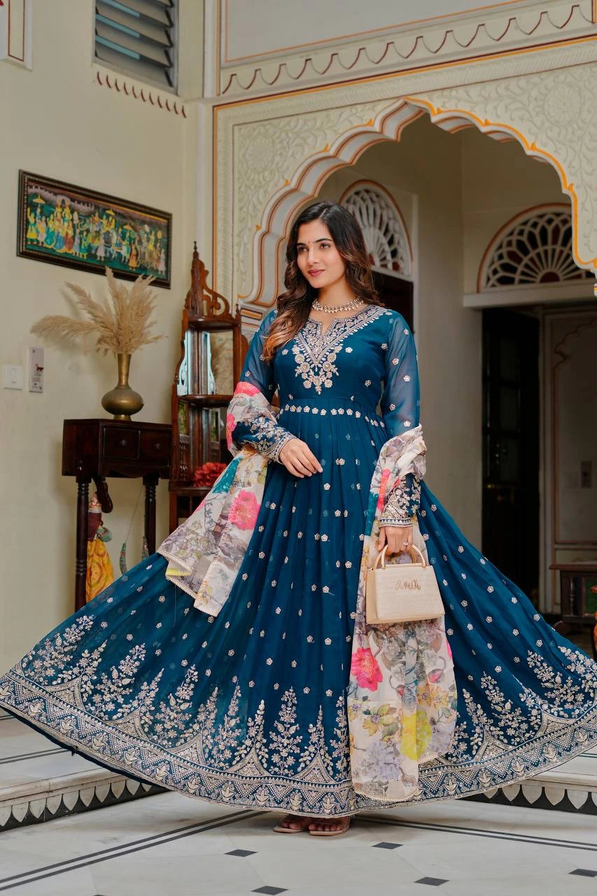 Woman in a blue embroidered traditional outfit standing in an ornate room.