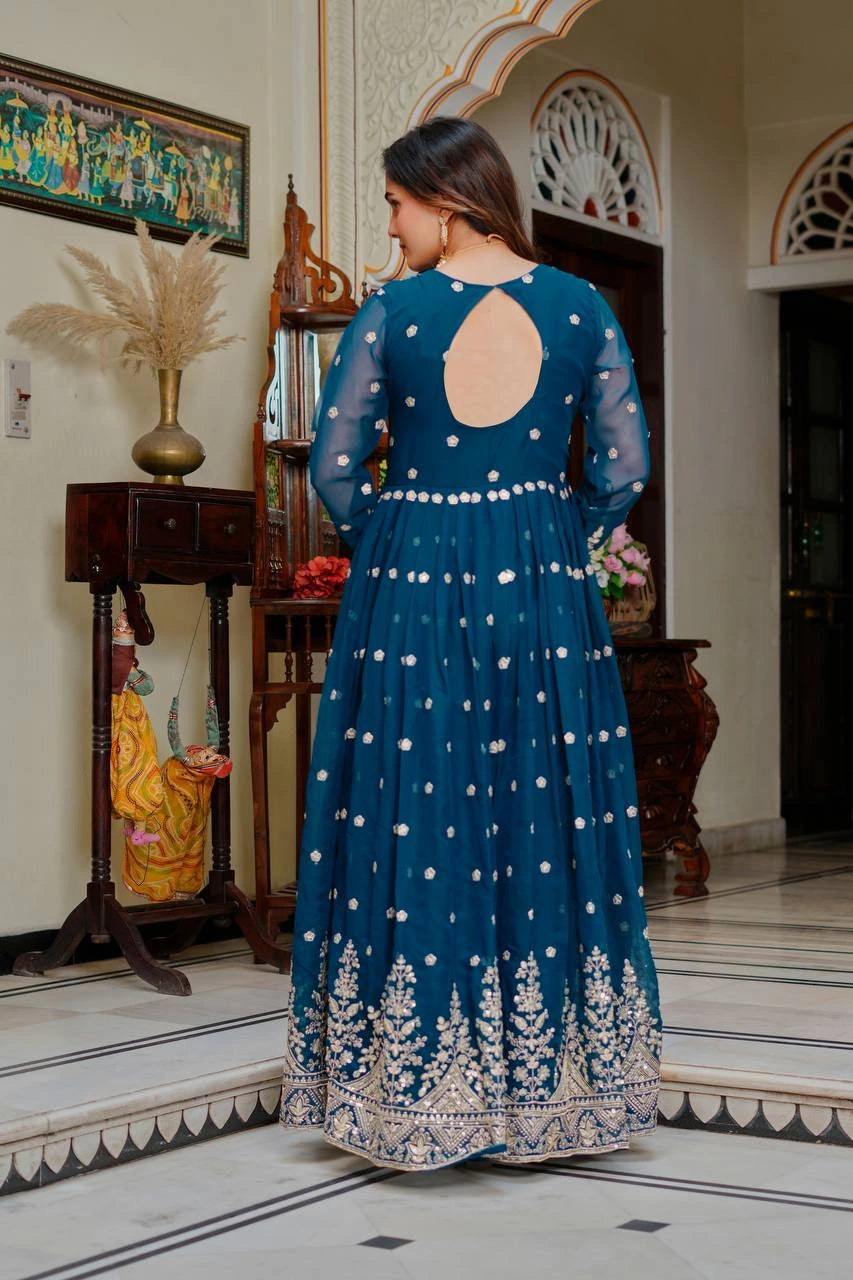 Woman in a blue embroidered dress standing in a decorated room.