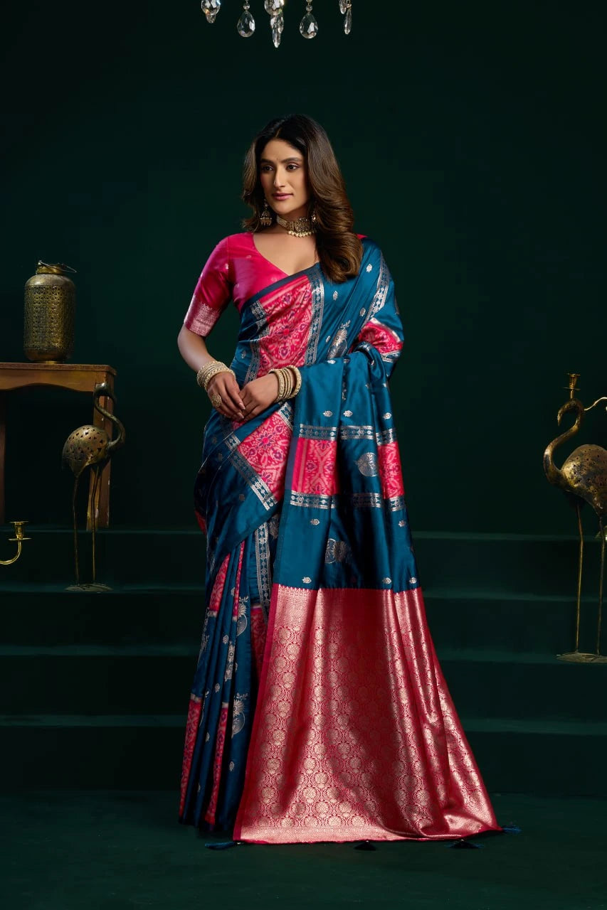 Woman in a blue and pink saree standing in a dark room with decorative elements.