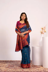 Woman wearing a colorful saree standing against a white wall with a vase of flowers.