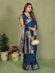 Woman in a blue saree with silver border standing against a green background