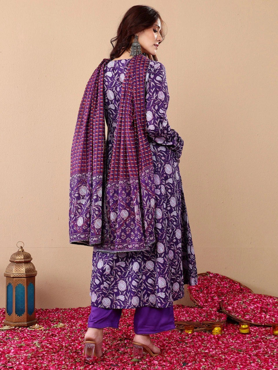 Woman wearing a purple and white patterned traditional outfit on a beige background with decorative elements.