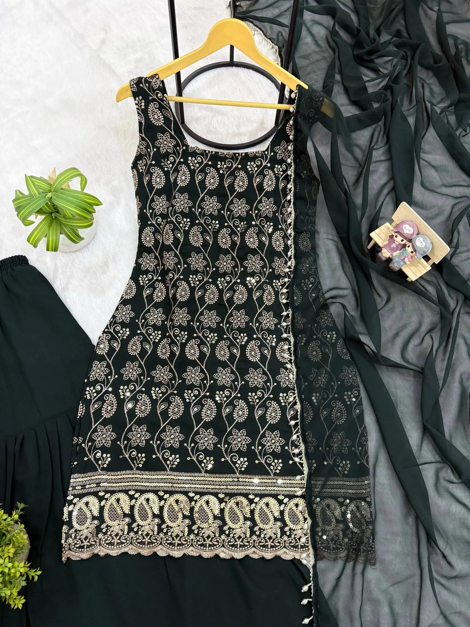 Black embroidered dress on a hanger with a gray fabric and green plant in the background