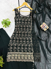 Black embroidered dress on a hanger with a gray fabric and green plant in the background