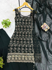 Black embroidered dress on a hanger with a gray fabric and green plant in the background