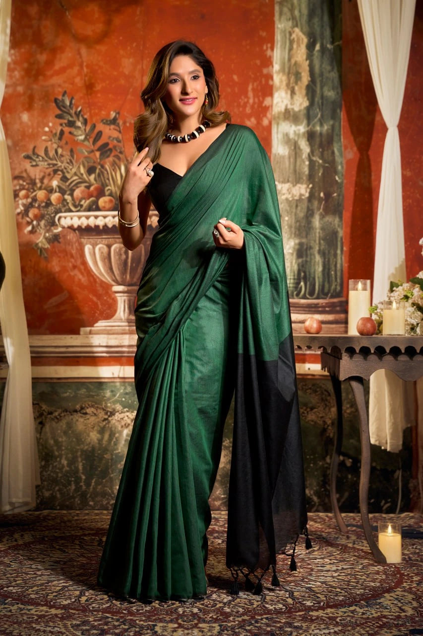 Woman in a green saree standing in a decorated room with floral wall art.