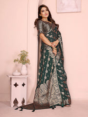 Woman wearing a dark green saree with a pattern, standing against a light pink wall.