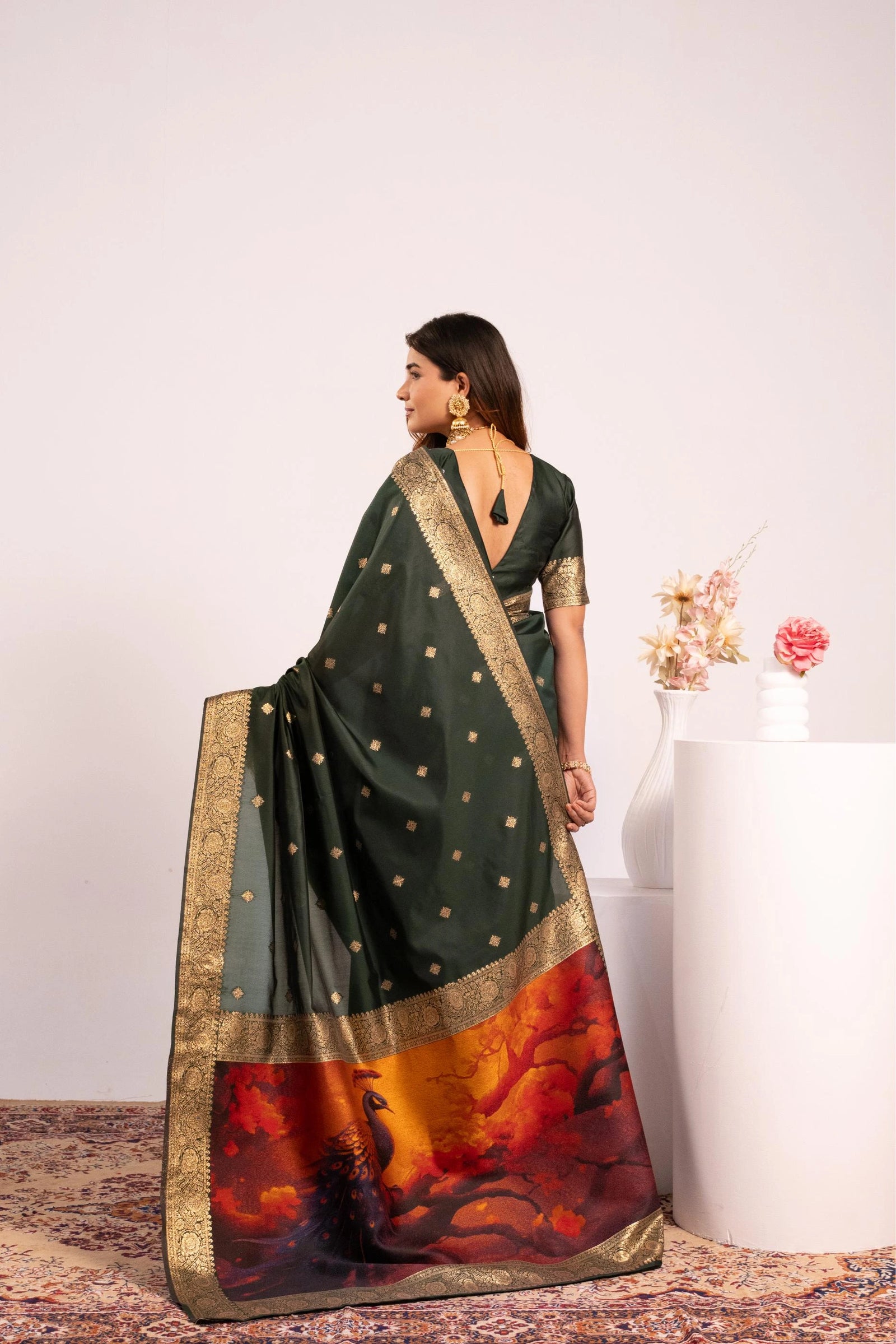 Woman wearing a dark green saree with a colorful pattern, standing against a white background.