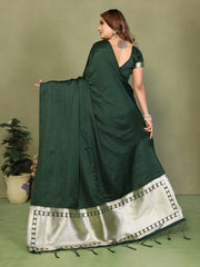 Woman wearing a dark green saree with a white border on a plain background