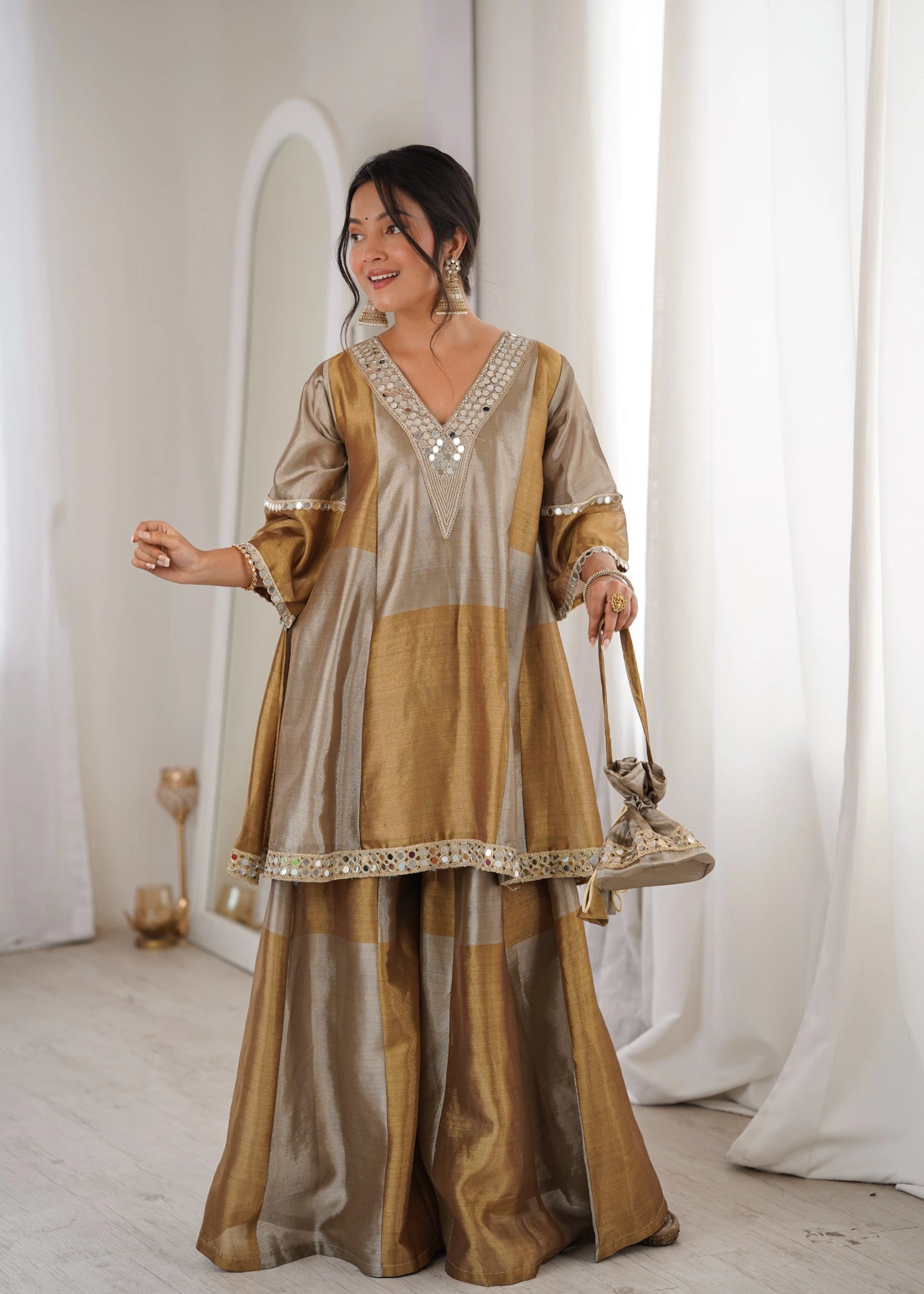 Woman in a traditional outfit standing in a softly lit room with white curtains.