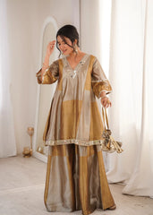 Woman wearing a traditional outfit with gold and beige colors in a softly lit room.