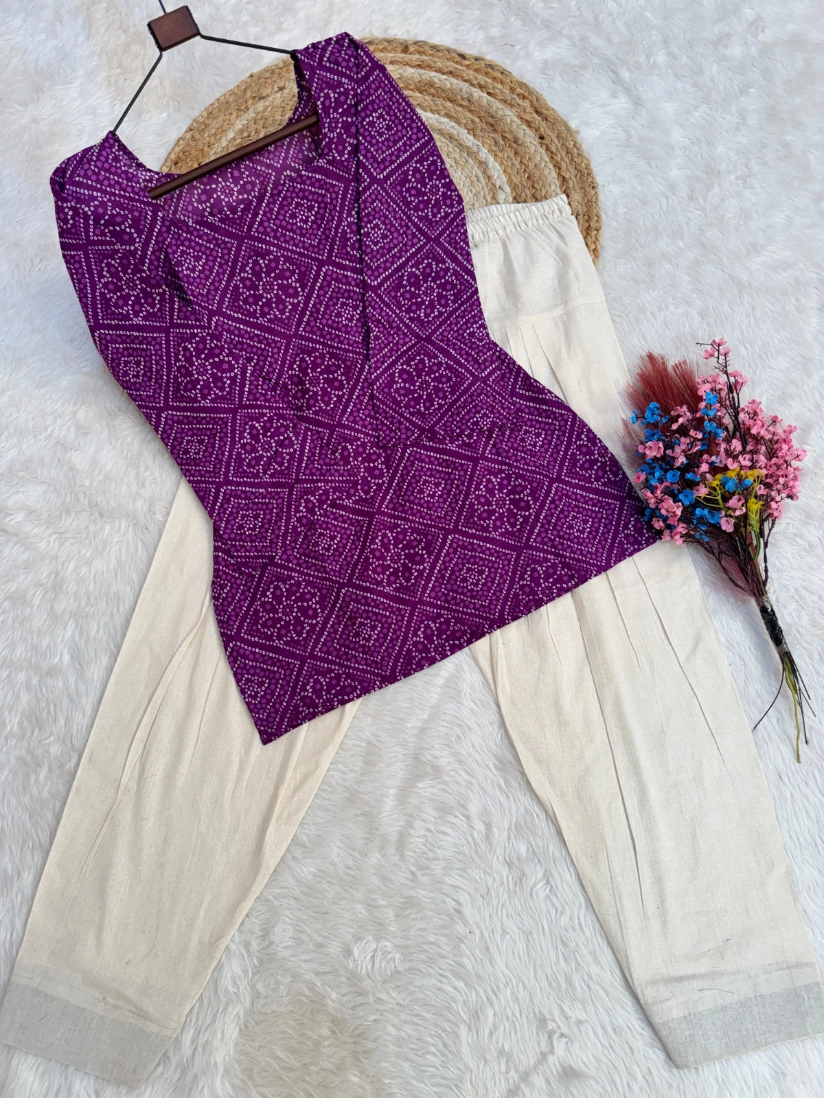 Purple patterned top and beige pants with a bouquet of flowers on a light gray background