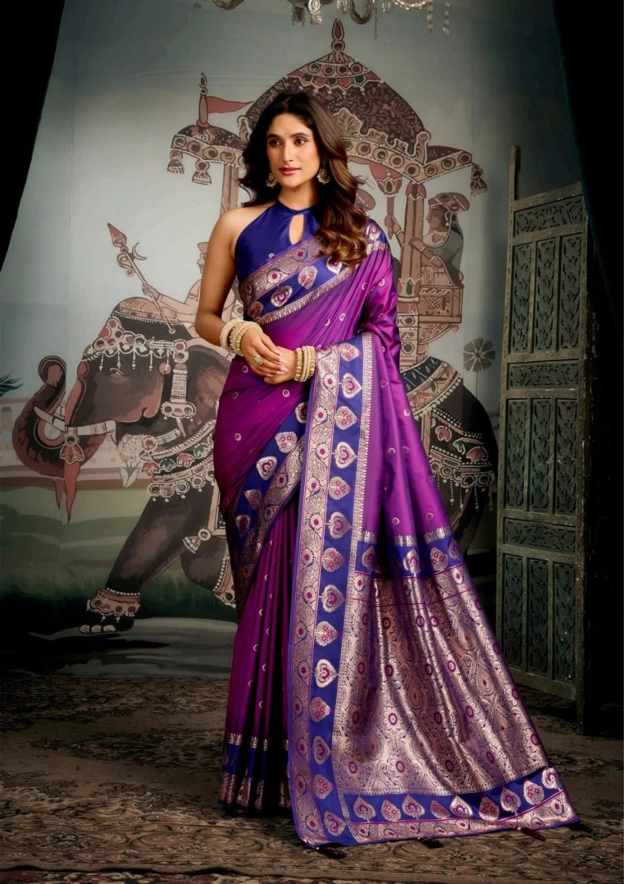 Woman in a purple and blue saree standing in front of an ornate wall design.