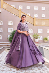 Woman in a purple traditional outfit standing in front of a decorative wall with plants.