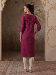 Woman wearing a magenta kurta with white patterns in an ornate room.