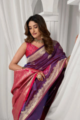 Woman wearing a traditional saree with a purple and pink design against a white curtain background
