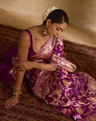 Woman in a traditional purple and gold saree sitting on a patterned rug.