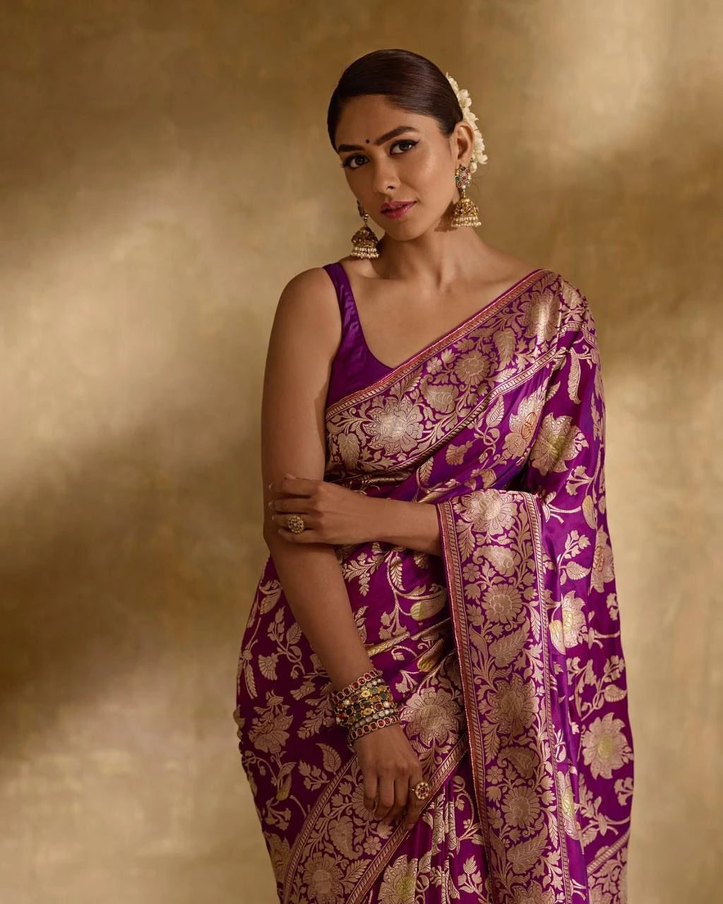 Woman wearing a purple saree with gold patterns against a beige background