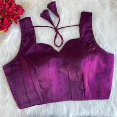 Purple top with tie straps on a white textured surface with red flowers.