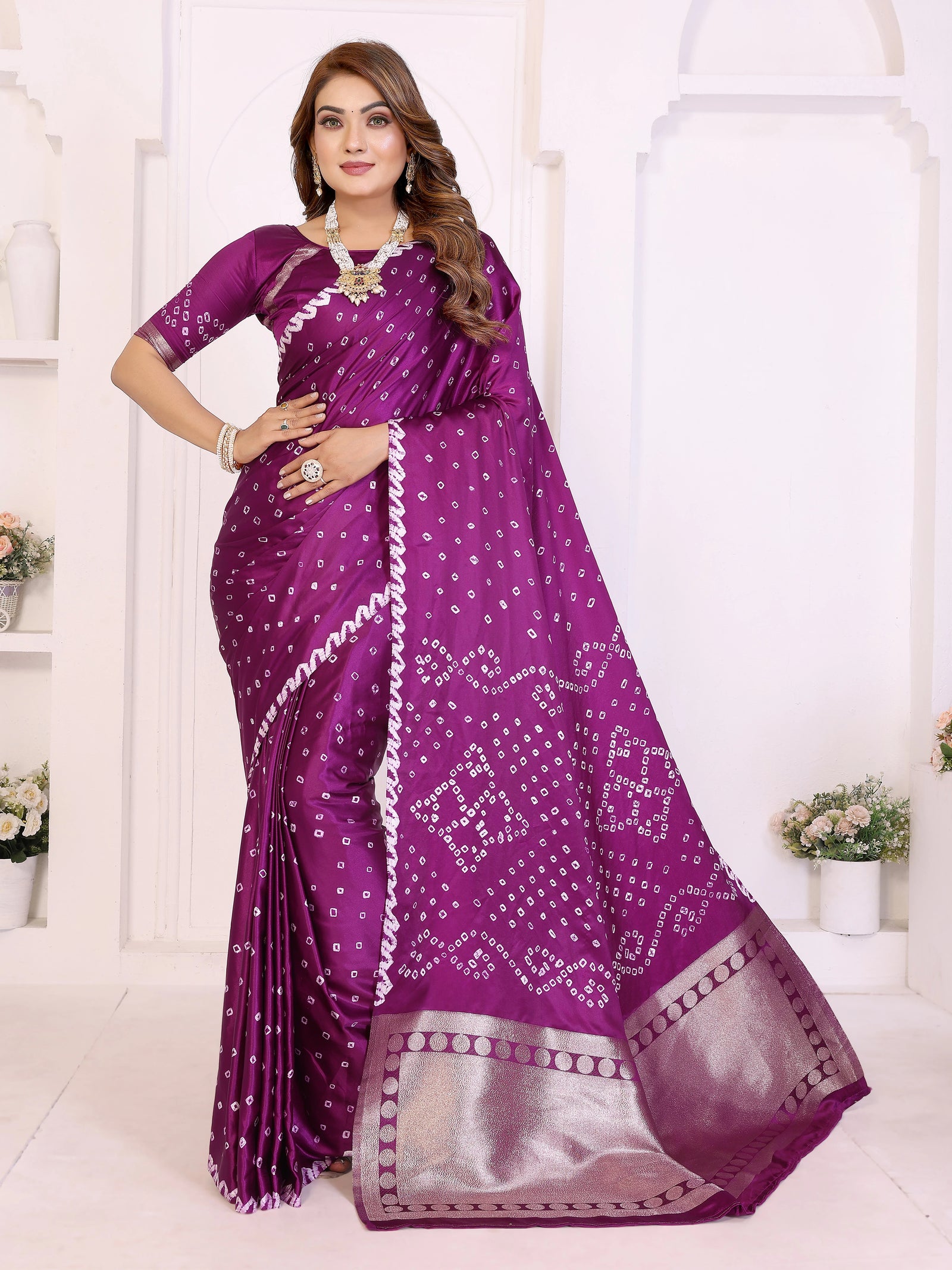 Woman wearing a purple saree with white patterns in a white room.