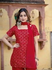 Woman wearing a red patterned outfit with a matching dupatta against a decorative wall.