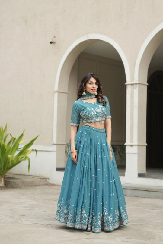 Woman in a teal traditional outfit standing in front of a building with arches.