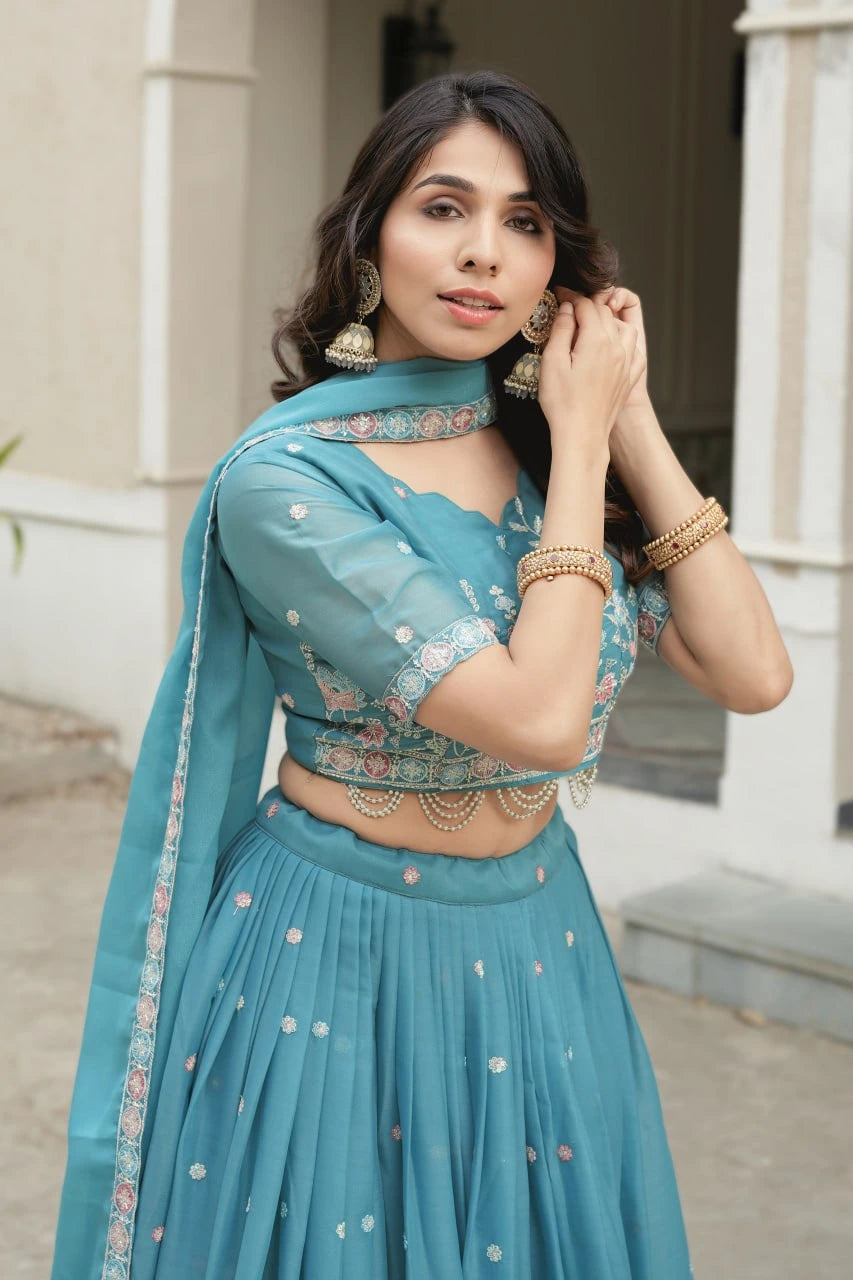 Woman wearing a teal traditional outfit with jewelry outdoors.