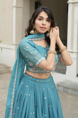 Woman wearing a teal traditional outfit with jewelry outdoors.