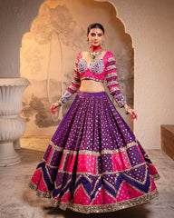 Woman wearing a traditional outfit with a pink blouse and purple skirt in an ornate setting.
