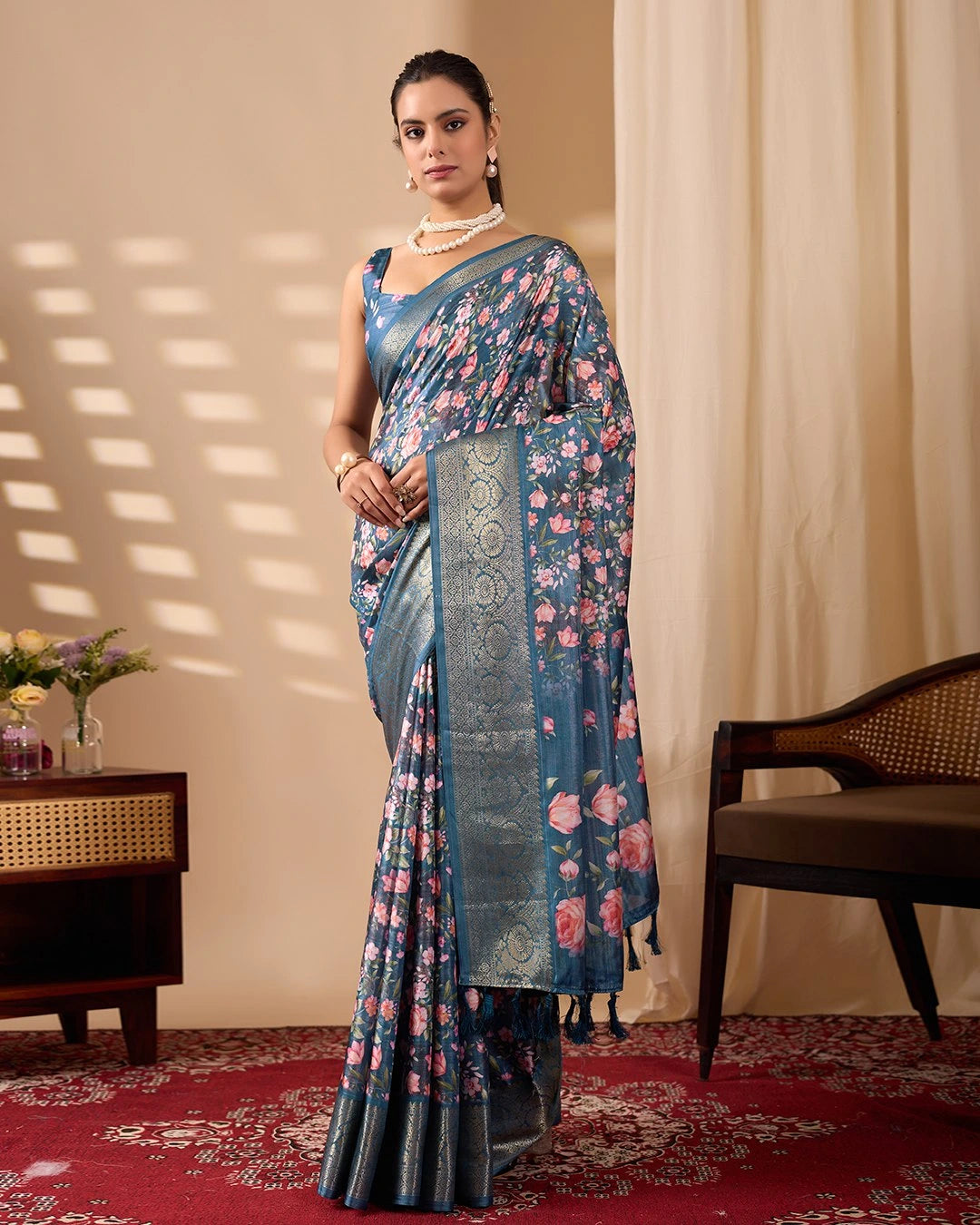 Woman wearing a floral saree standing in a room with a beige wall and red carpet.