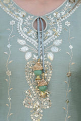 Decorative neckline of a garment with intricate beadwork and embroidery on a light blue background.
