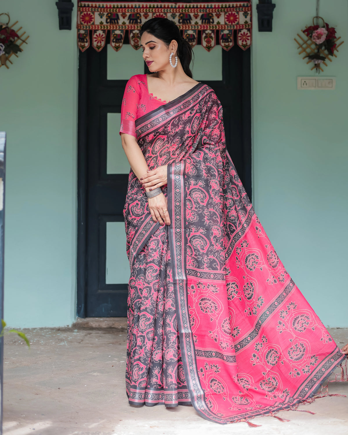Woman wearing a pink and black saree in front of a door with decorative elements.