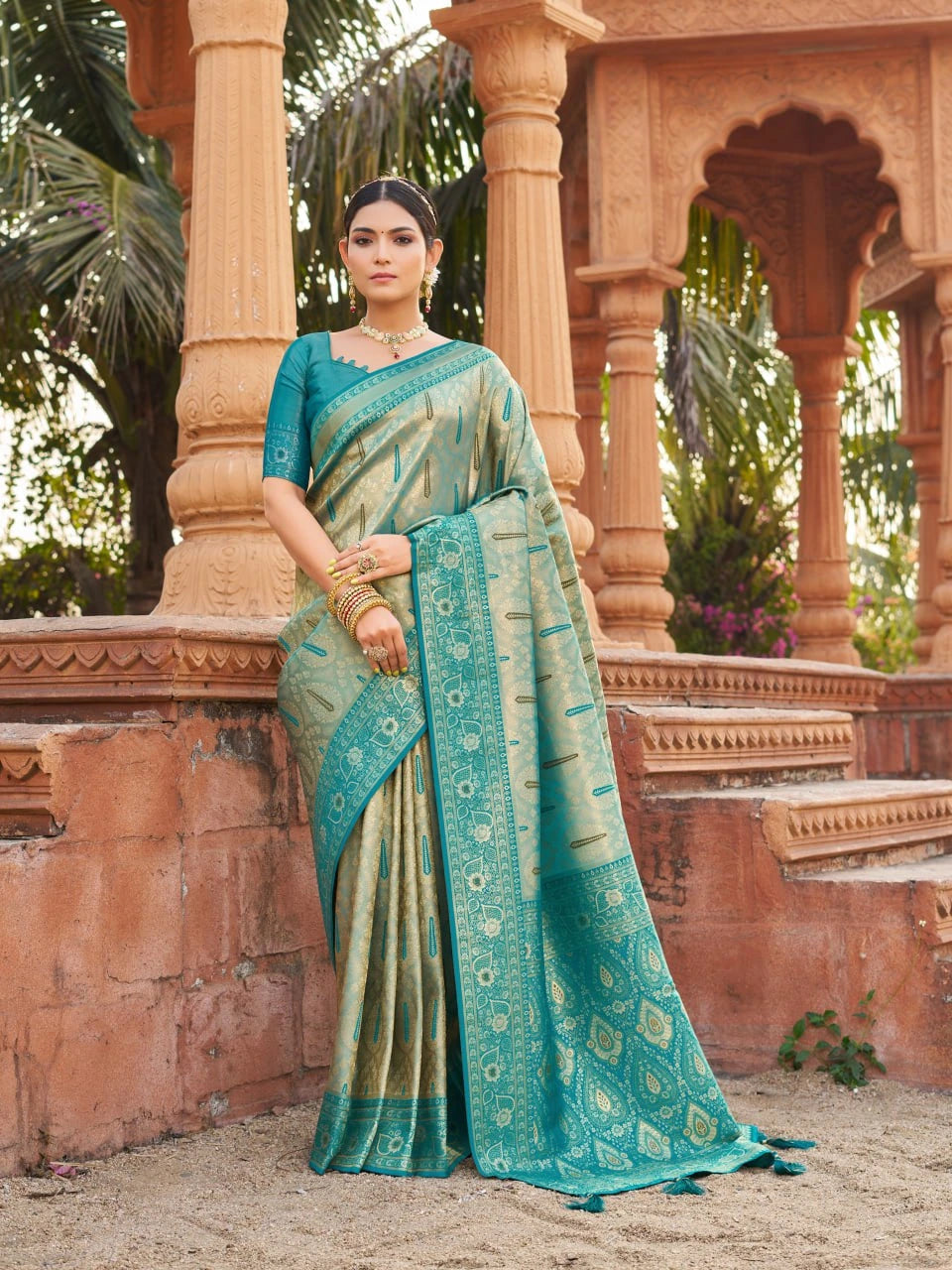 Woman in a teal saree standing in front of an architectural structure with columns.