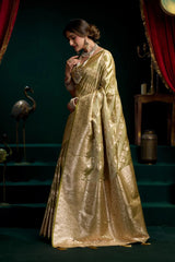 Woman in a gold saree standing in a dimly lit room with red curtains.