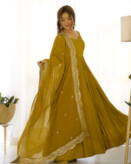 Woman wearing a mustard yellow dress with white embroidery in a bright room.