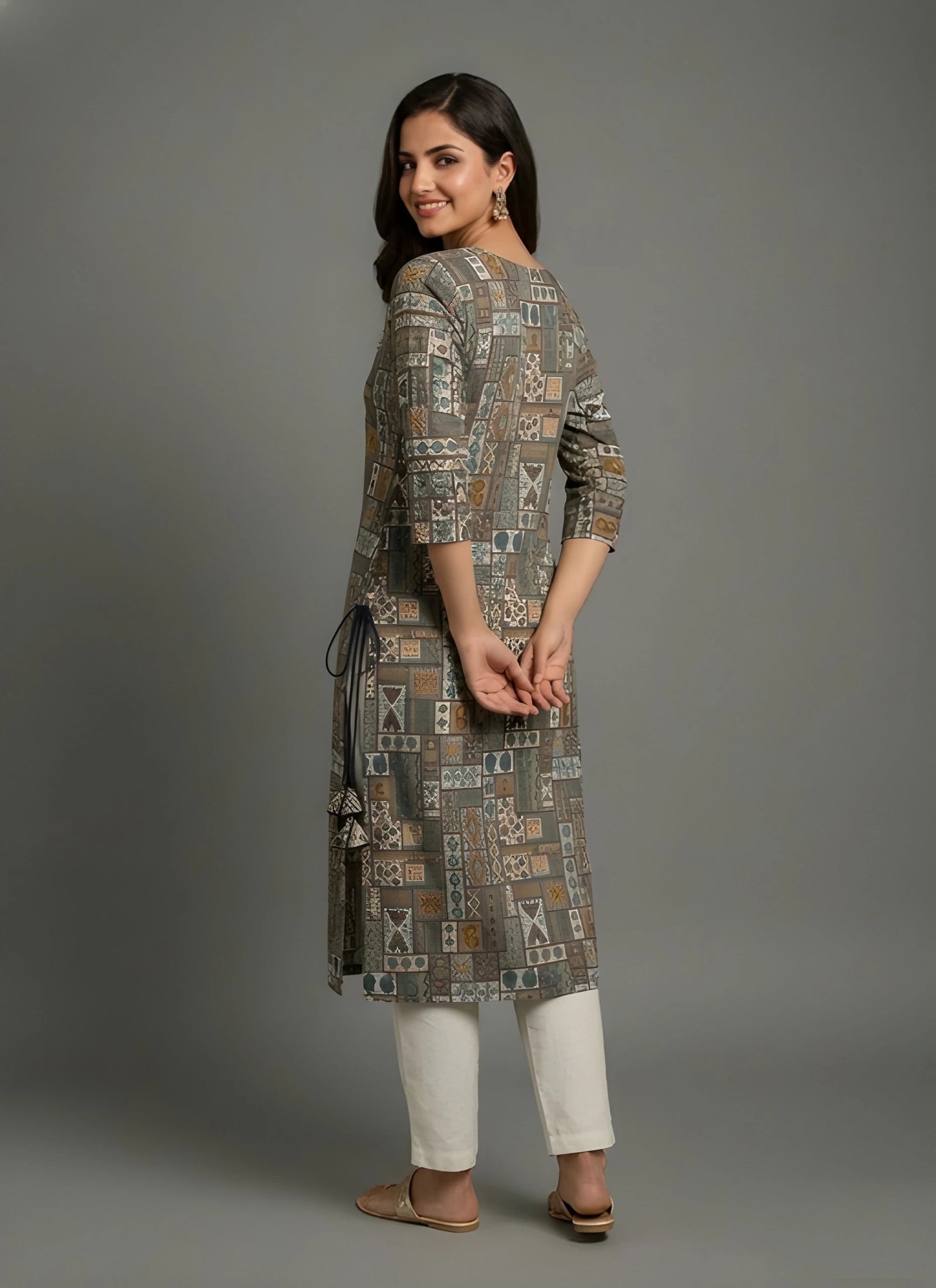 Woman wearing a patterned long dress with white pants on a gray background