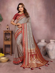 Woman wearing a traditional saree with red and gold patterns in a decorative setting.