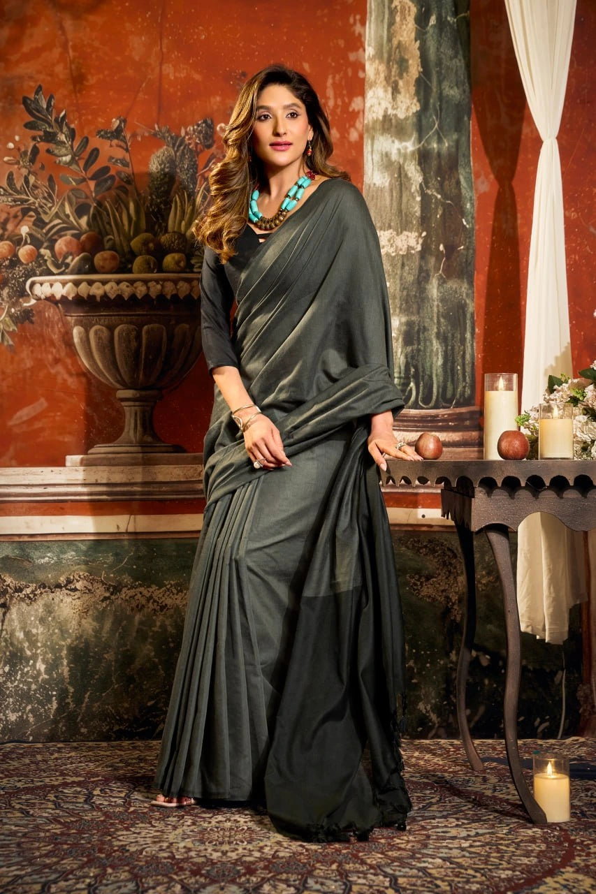 Woman in a dark green saree standing in an ornate room with classical decor.