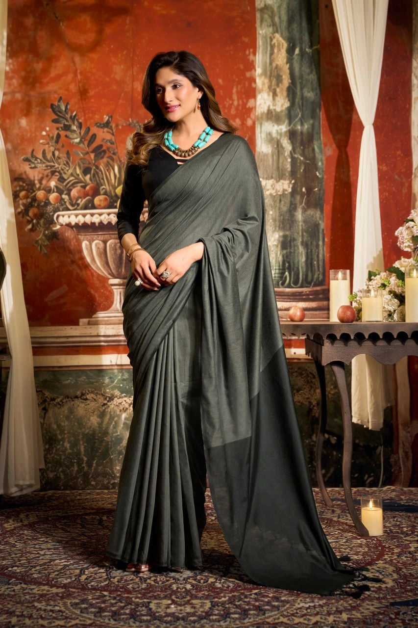 Woman in a dark green saree standing in an ornate room with red walls and decorative elements.