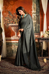 Woman in a dark gray saree standing in an ornate room with red walls and decorative elements.