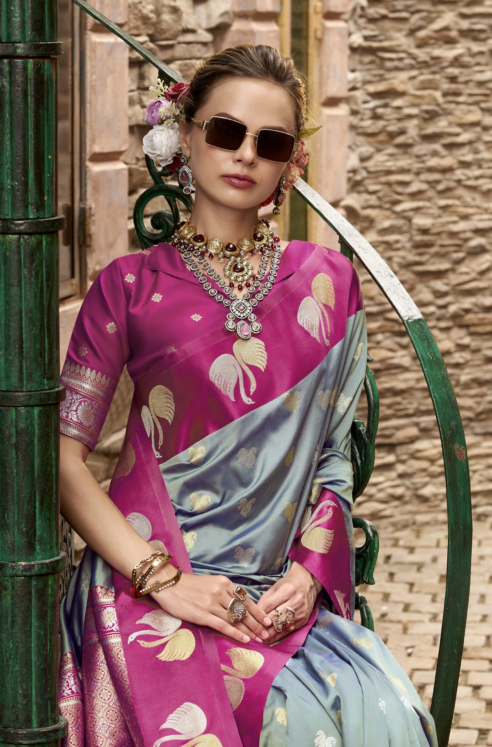 Woman wearing a pink and blue saree with elephant patterns, standing against a textured wall.
