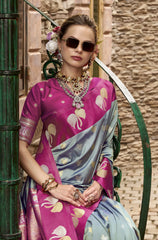 Woman wearing a pink and blue saree with elephant patterns, standing against a textured wall.