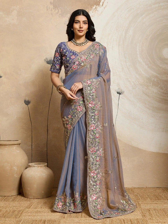 Woman wearing a blue saree with floral patterns against a neutral background