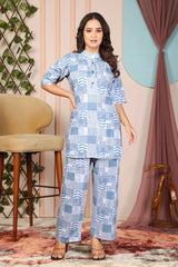 Woman wearing a blue patterned outfit standing in a room with decorative elements.