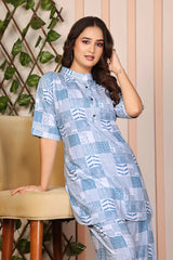 Woman wearing a blue patterned dress sitting on a chair with a decorative wall in the background