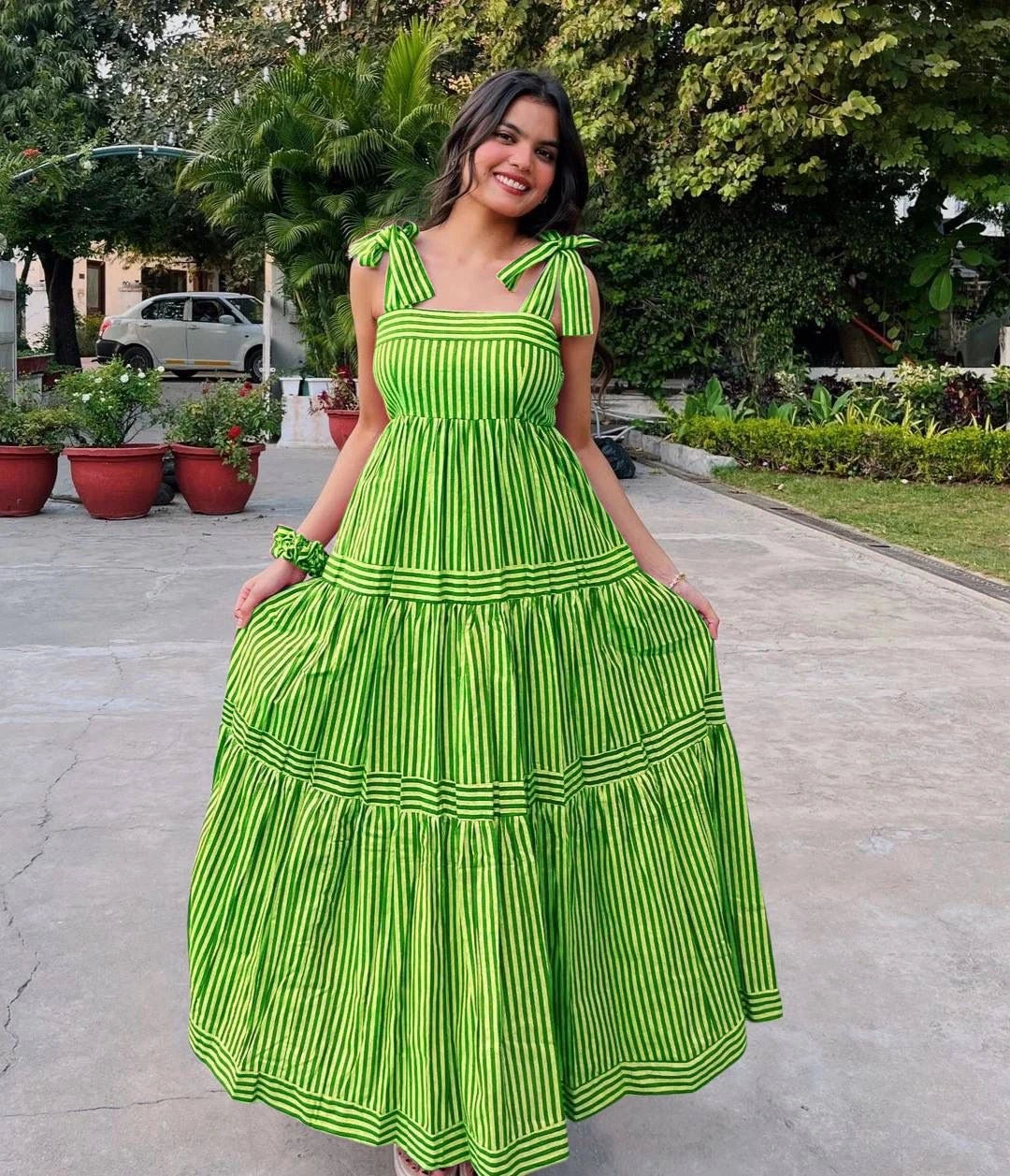 Woman wearing a green and white striped dress in an outdoor setting with plants and a car in the background.