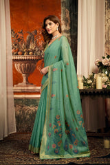Woman wearing a green saree with floral patterns in an elegant indoor setting.