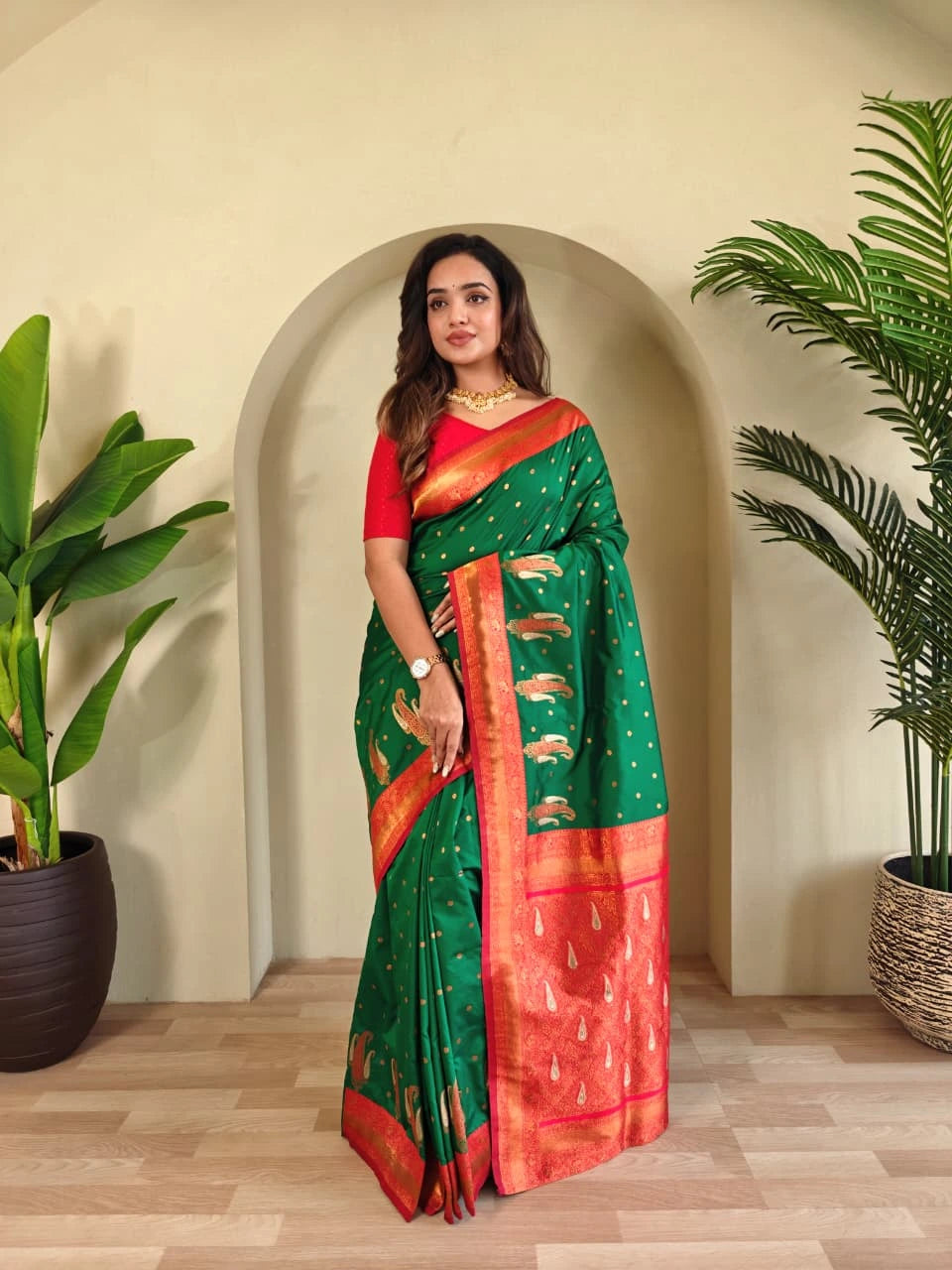 Woman wearing a green and red saree with a plant in the background