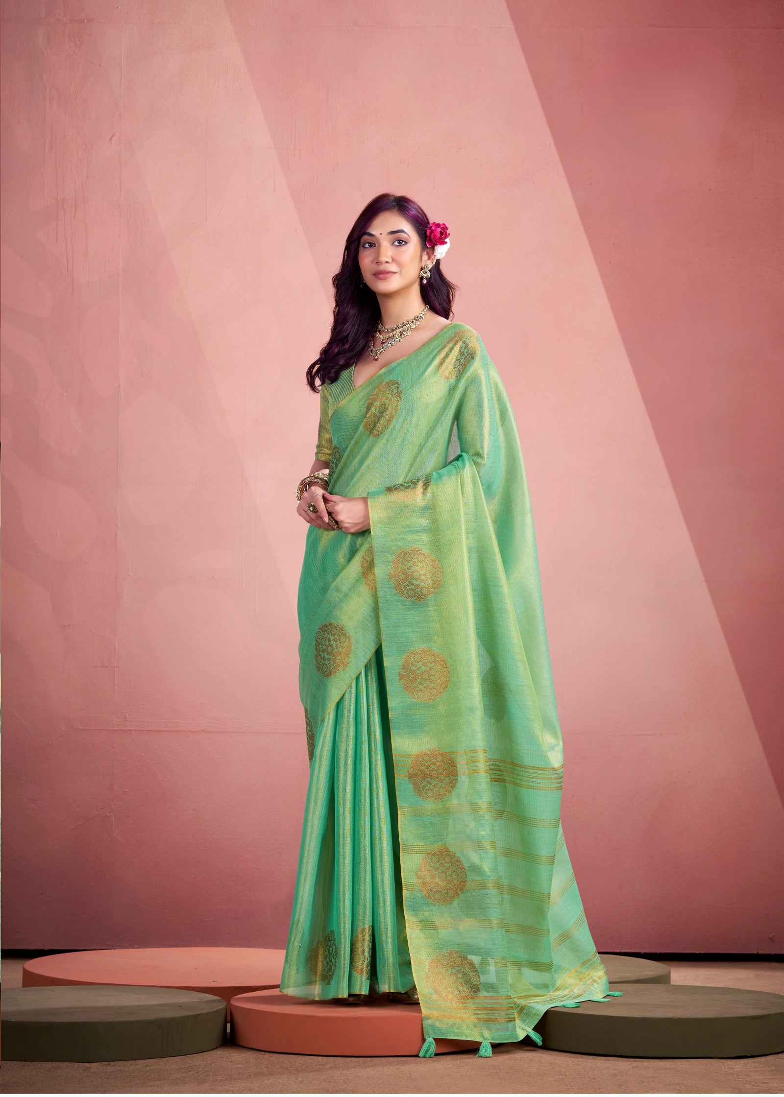 Woman wearing a green saree with gold patterns against a pink background